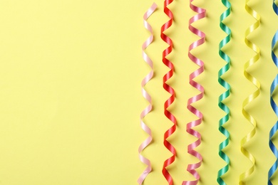 Photo of Colorful serpentine streamers on yellow background, flat lay. Space for text