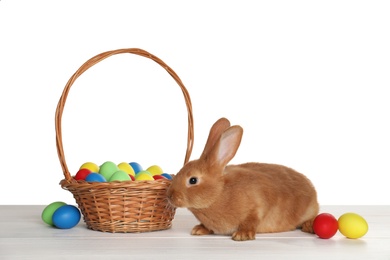 Photo of Cute fluffy bunny, wicker basket and Easter eggs on white wooden table