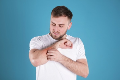 Photo of Man scratching forearm on color background. Allergy symptoms