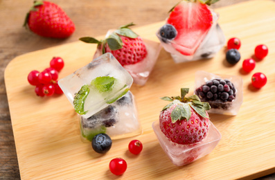 Ice cubes with different berries and mint on wooden board, closeup