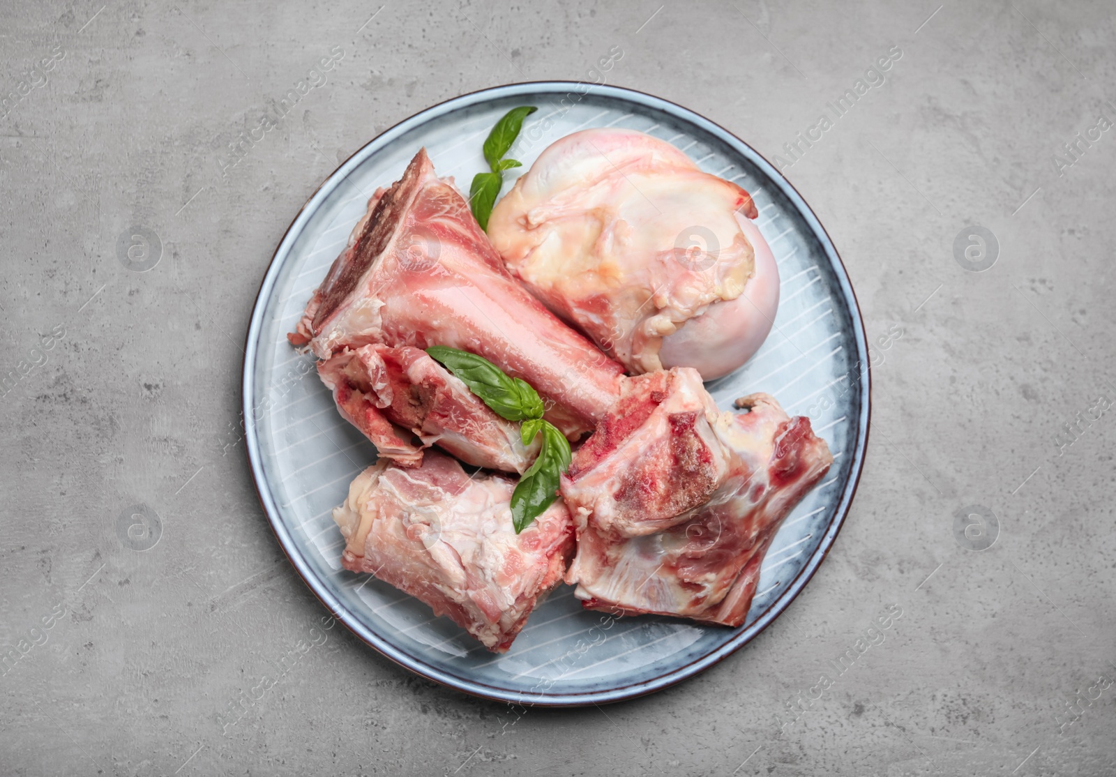 Photo of Plate with raw chopped meaty bones and basil on grey table, top view