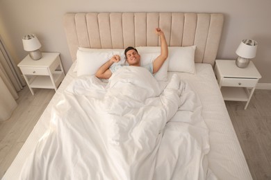 Man stretching in bed with white linens at home