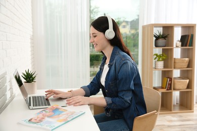 Photo of Teenage girl with headphones working on laptop at home