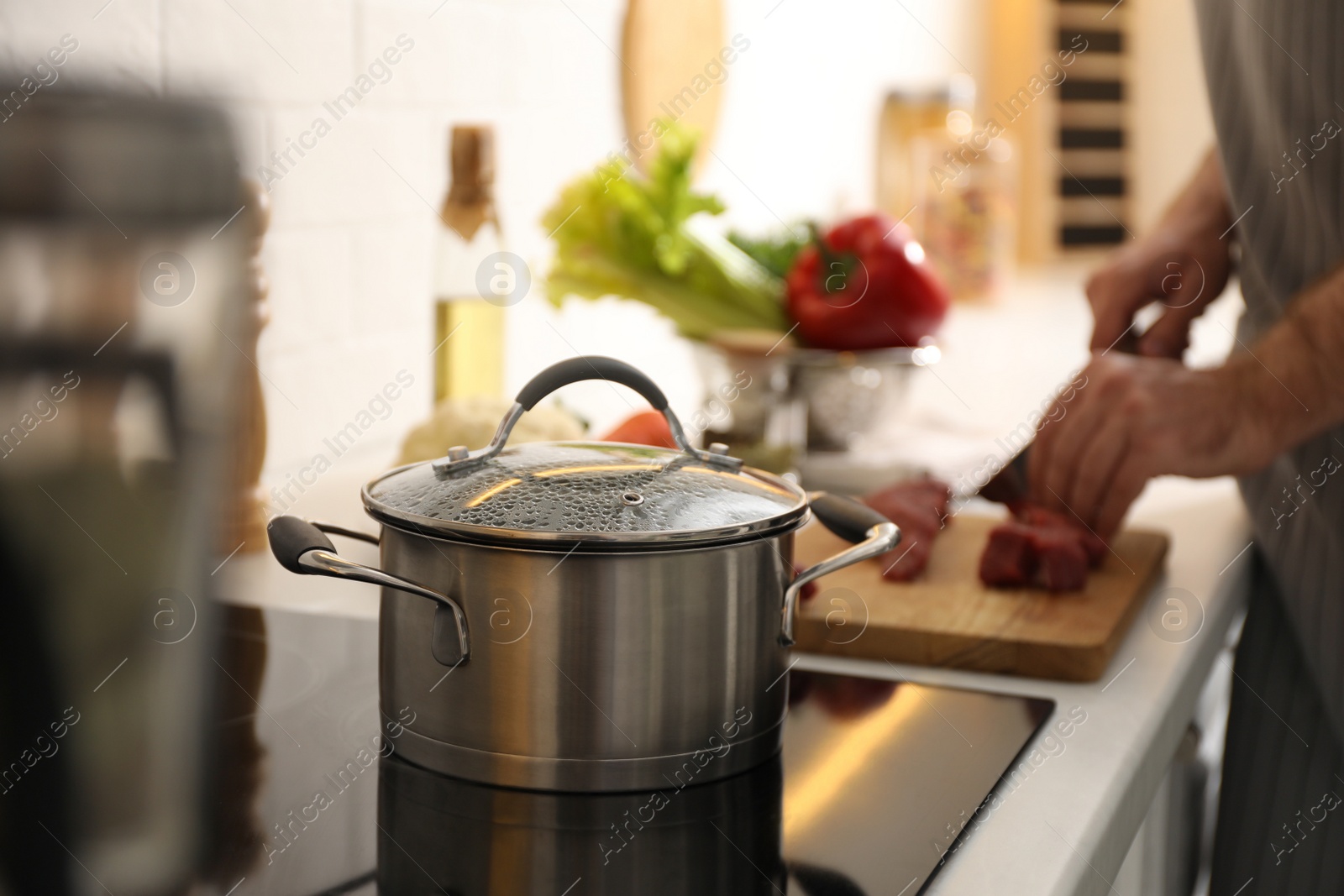 Photo of Homemade bouillon recipe. Man cutting meat in kitchen, focus on pot