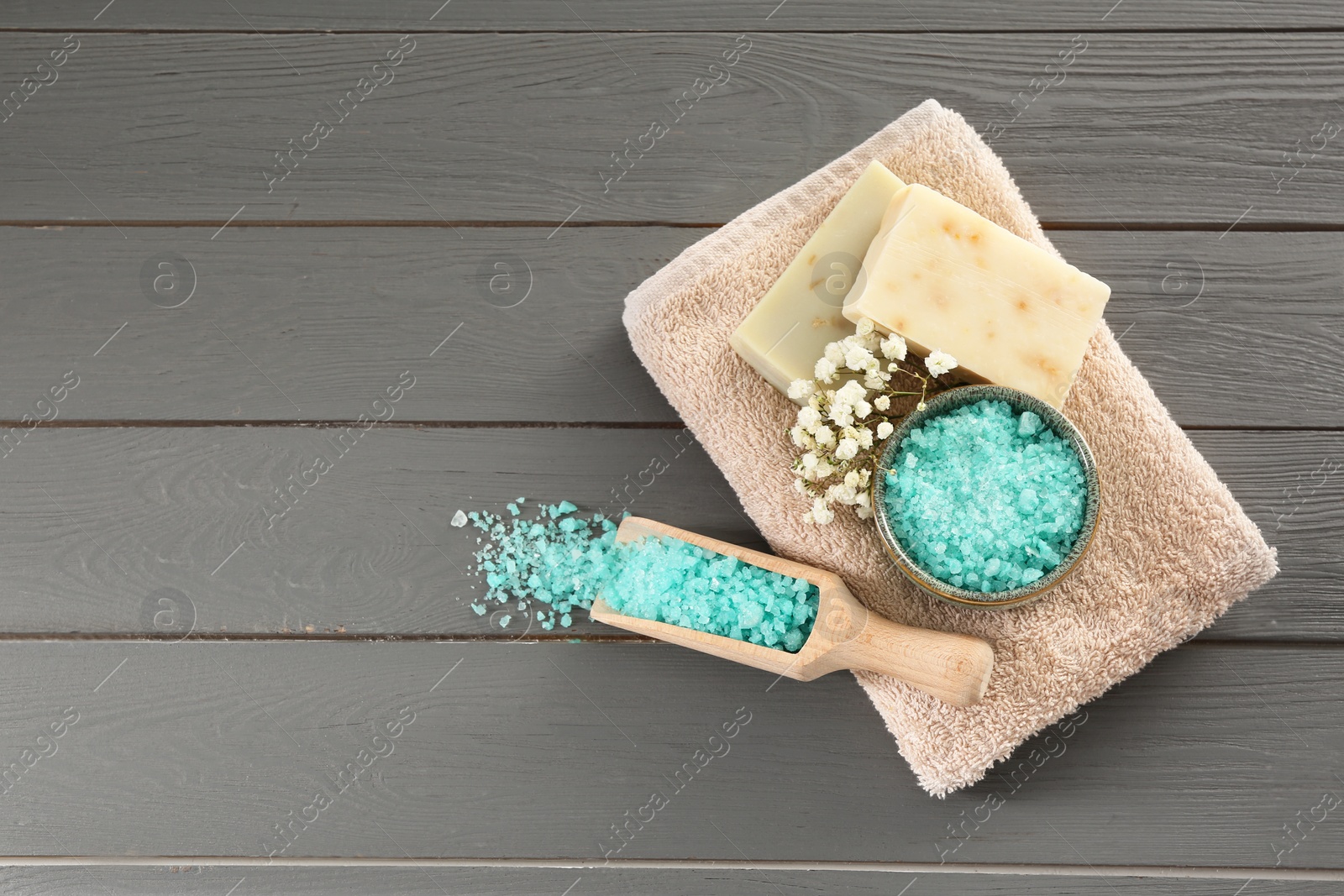 Photo of Aromatic sea salt and beautiful flowers on grey wooden table, flat lay. Space for text