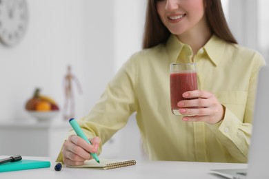 Photo of Beautiful young woman with delicious smoothie while working at table, closeup