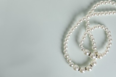 Photo of Elegant pearl necklace and bracelet on white table, top view. Space for text