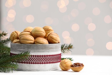 Homemade walnut shaped cookies with boiled condensed milk near fir branches on white table, space for text. Bokeh effect
