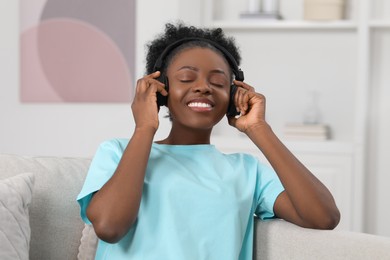 Photo of Beautiful young woman in headphones enjoying music on sofa indoors