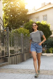 Photo of Beautiful young woman in stylish sunglasses walking on city street