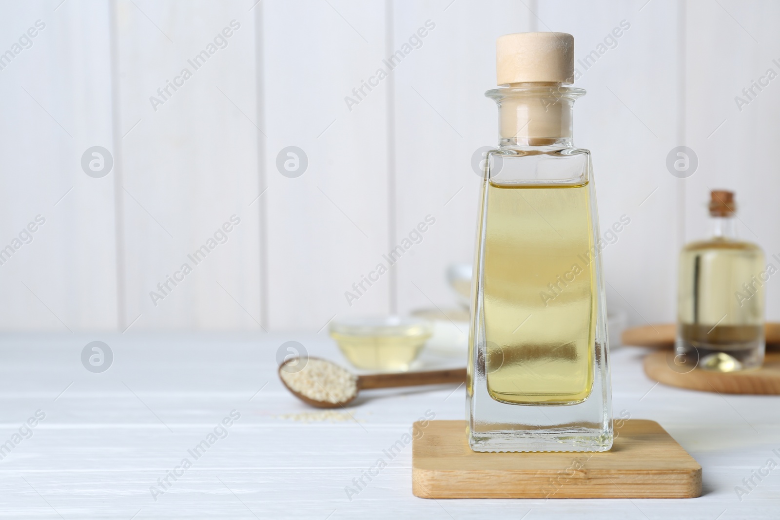 Photo of Glass bottle of sesame oil and seeds on white wooden table. Space for text