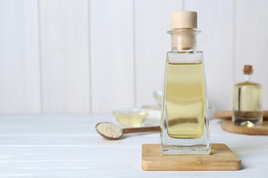 Glass bottle of sesame oil and seeds on white wooden table. Space for text