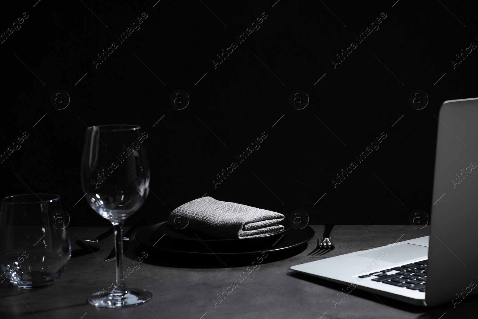 Photo of Composition with tableware and laptop on table against black background, space for text. Loneliness concept
