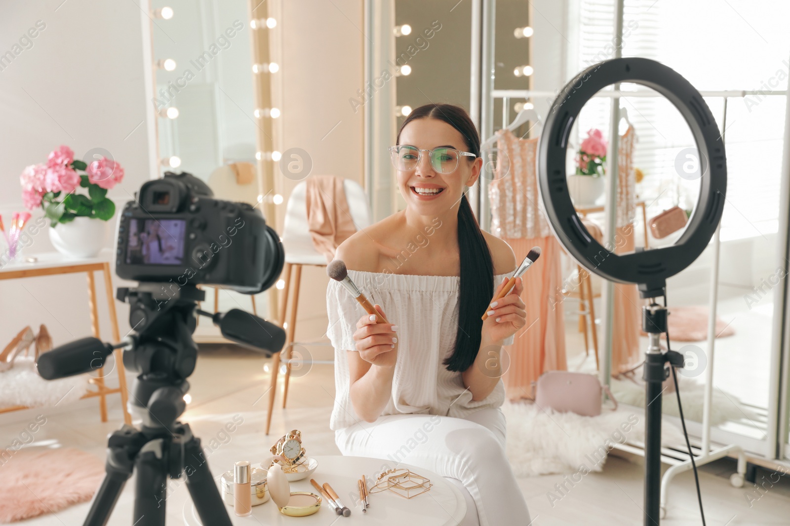 Photo of Blogger with brushes recording video in dressing room at home. Using ring lamp and camera