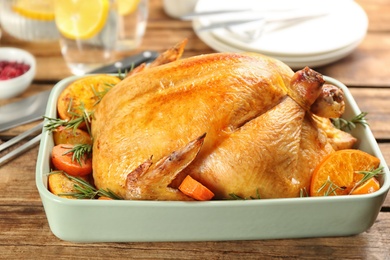 Photo of Roasted chicken with oranges and carrot on wooden table, closeup