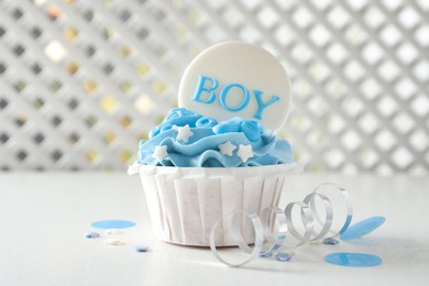 Photo of Delicious cupcake with light blue cream and Boy topper for baby shower on white table