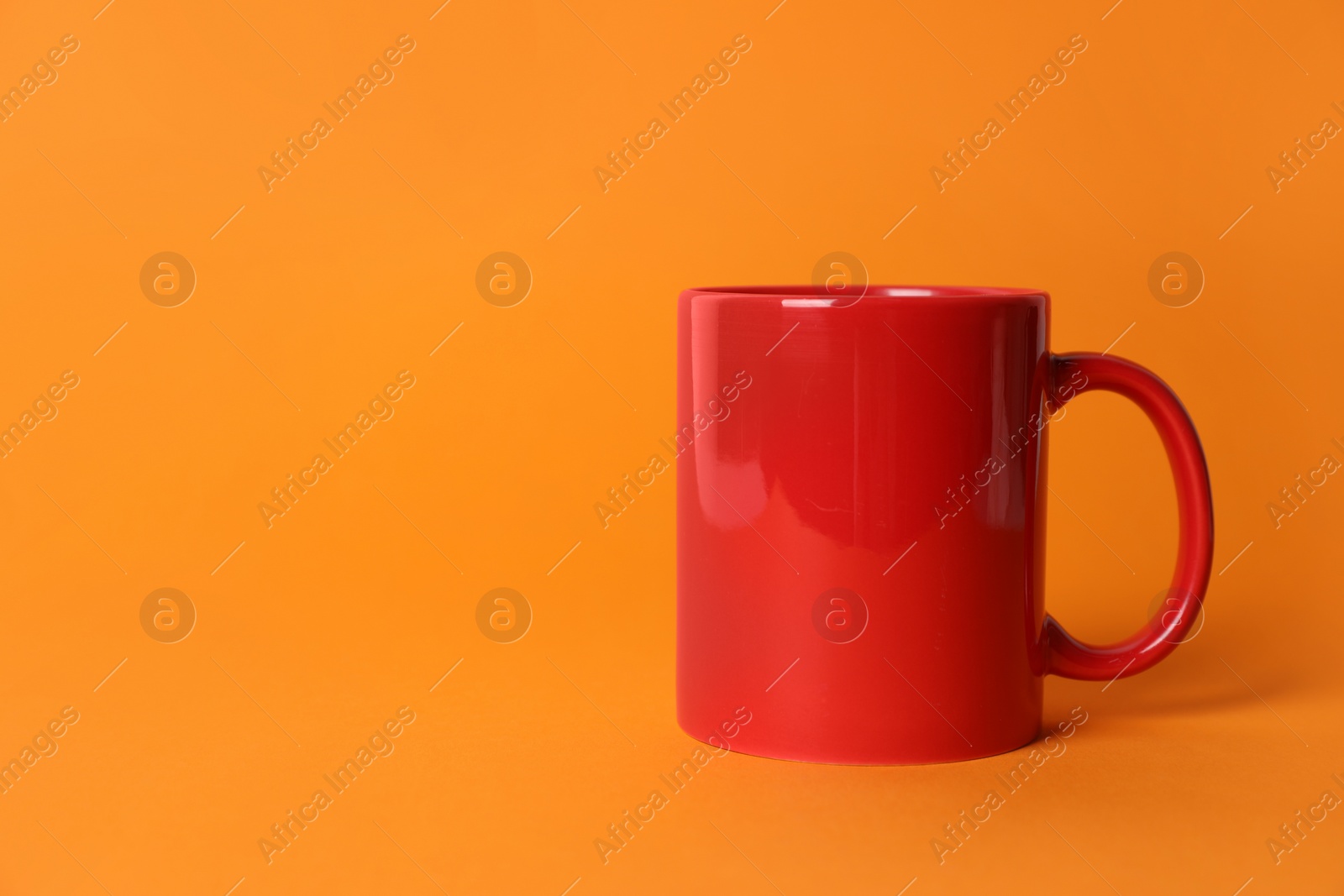 One red ceramic mug on orange background. Space for text Photo of One red ceramic mug on orange background. Space for text