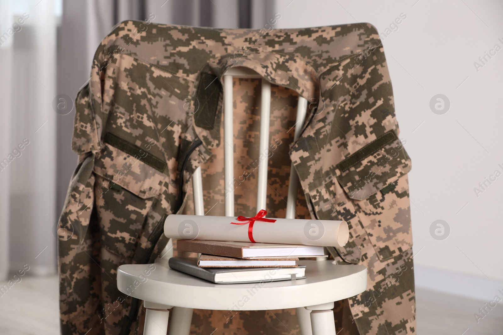 Photo of Chair with soldier uniform, notebooks and diploma indoors. Military education