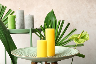 Photo of Creative composition with candles and tropical plants on color background