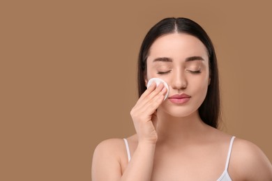 Photo of Beautiful woman removing makeup with cotton pad on beige background, space for text