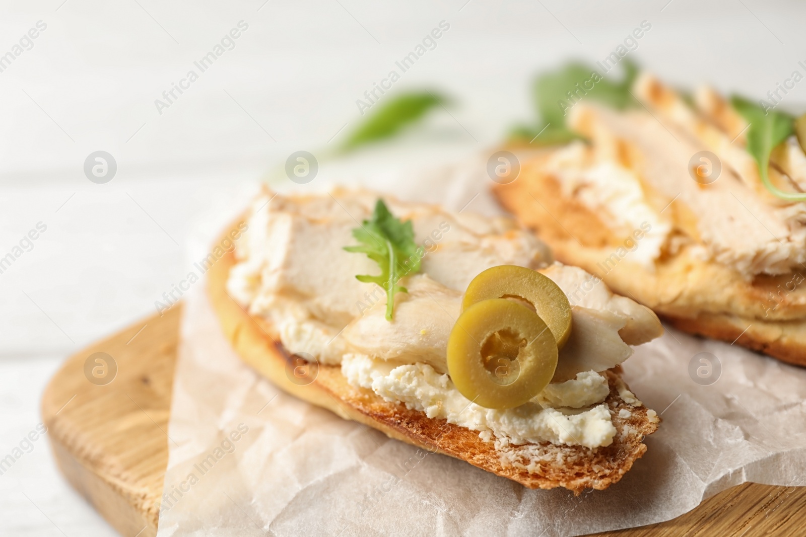 Photo of Board with delicious chicken bruschettas on white wooden table, closeup