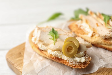 Board with delicious chicken bruschettas on white wooden table, closeup