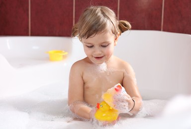 Photo of Little girl bathing with toy ducks in tub