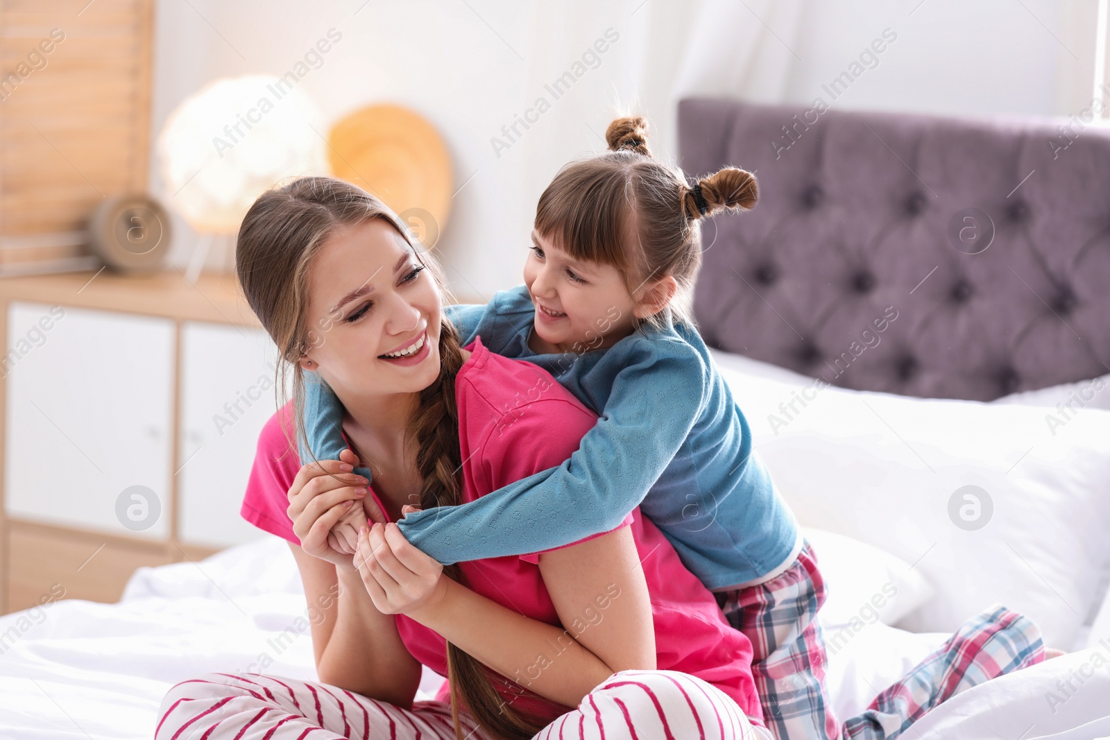 Photo of Happy woman and daughter in pajamas on bed at home