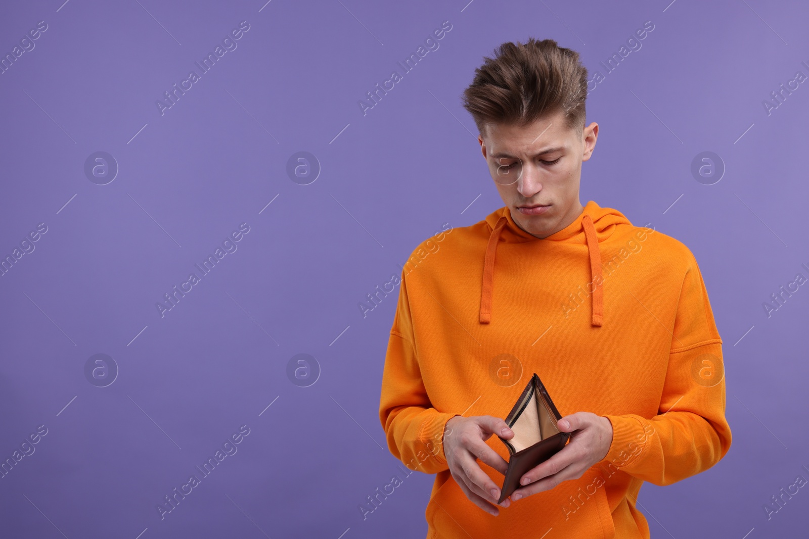 Photo of Upset man looking at his empty wallet on purple background. Space for text