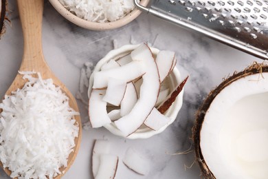 Photo of Coconut flakes, pieces, spoon and grater on white marble table, flat lay