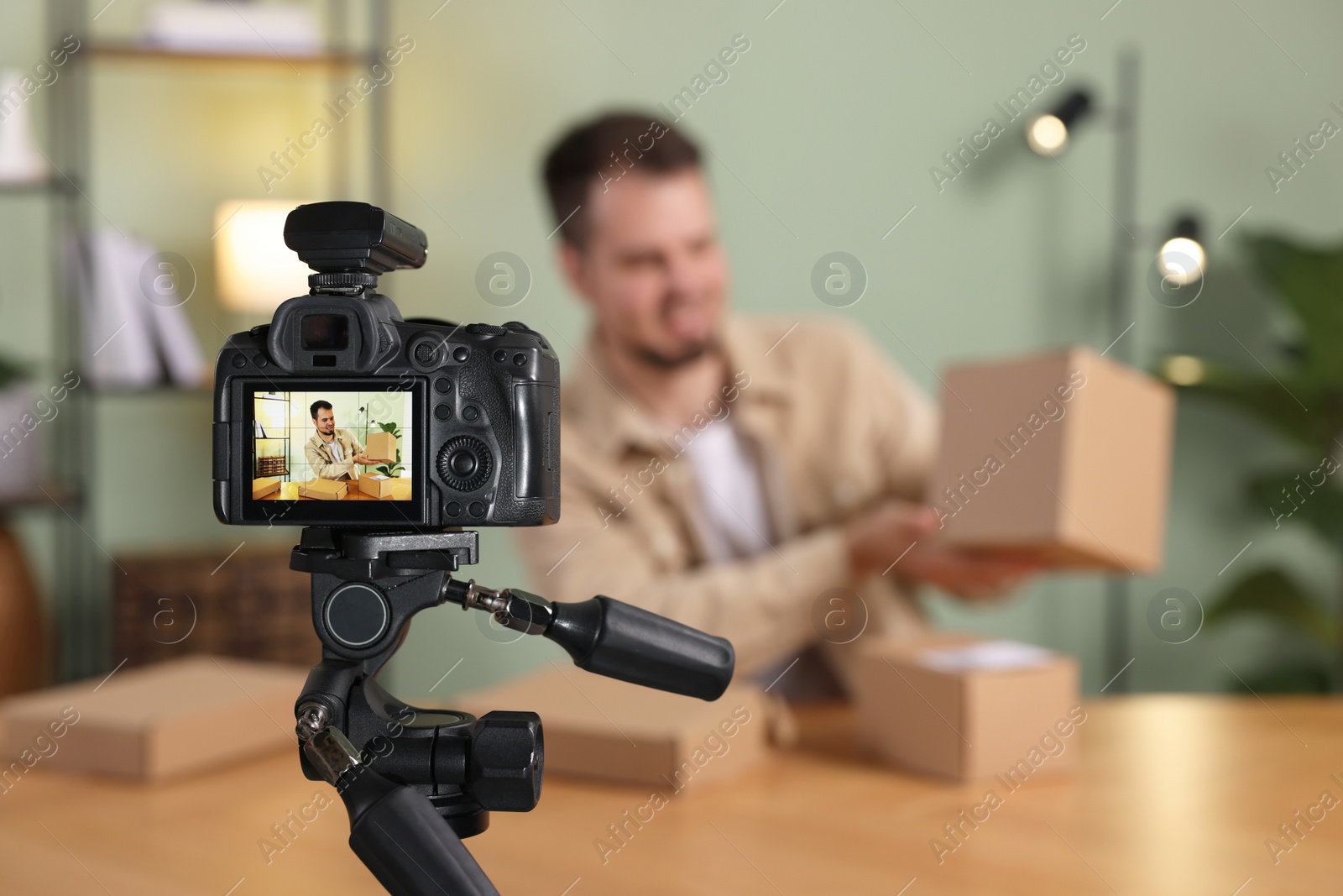 Photo of Blogger with many parcels recording video at home, focus on camera