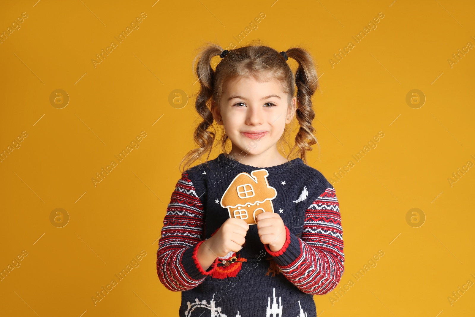 Photo of Cute little girl with Christmas gingerbread cookie on yellow background