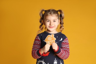 Cute little girl with Christmas gingerbread cookie on yellow background