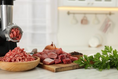 Photo of Electric meat grinder with beef and products on white marble table in kitchen