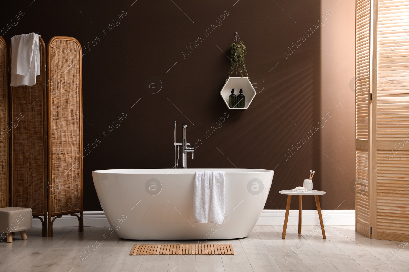 Photo of Modern ceramic bathtub with towel near brown wall in room