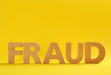 Word Fraud made of wooden letters on yellow background, space for text