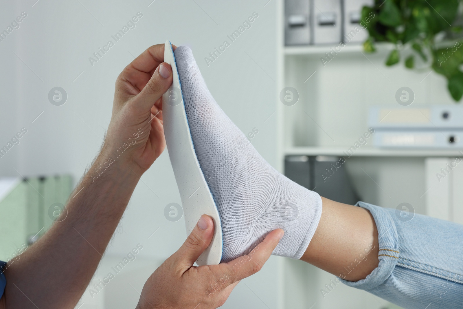 Photo of Male orthopedist fitting insole to patient's foot in hospital, closeup