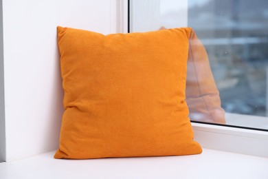 Photo of Orange soft pillow on window sill indoors