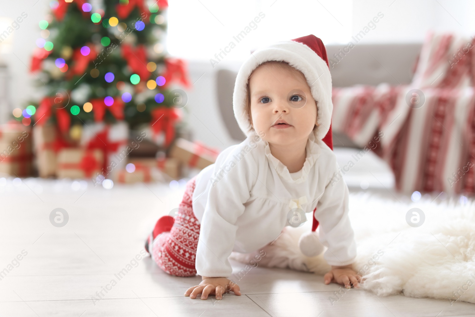 Photo of Cute baby in Santa hat on floor at home. Christmas celebration