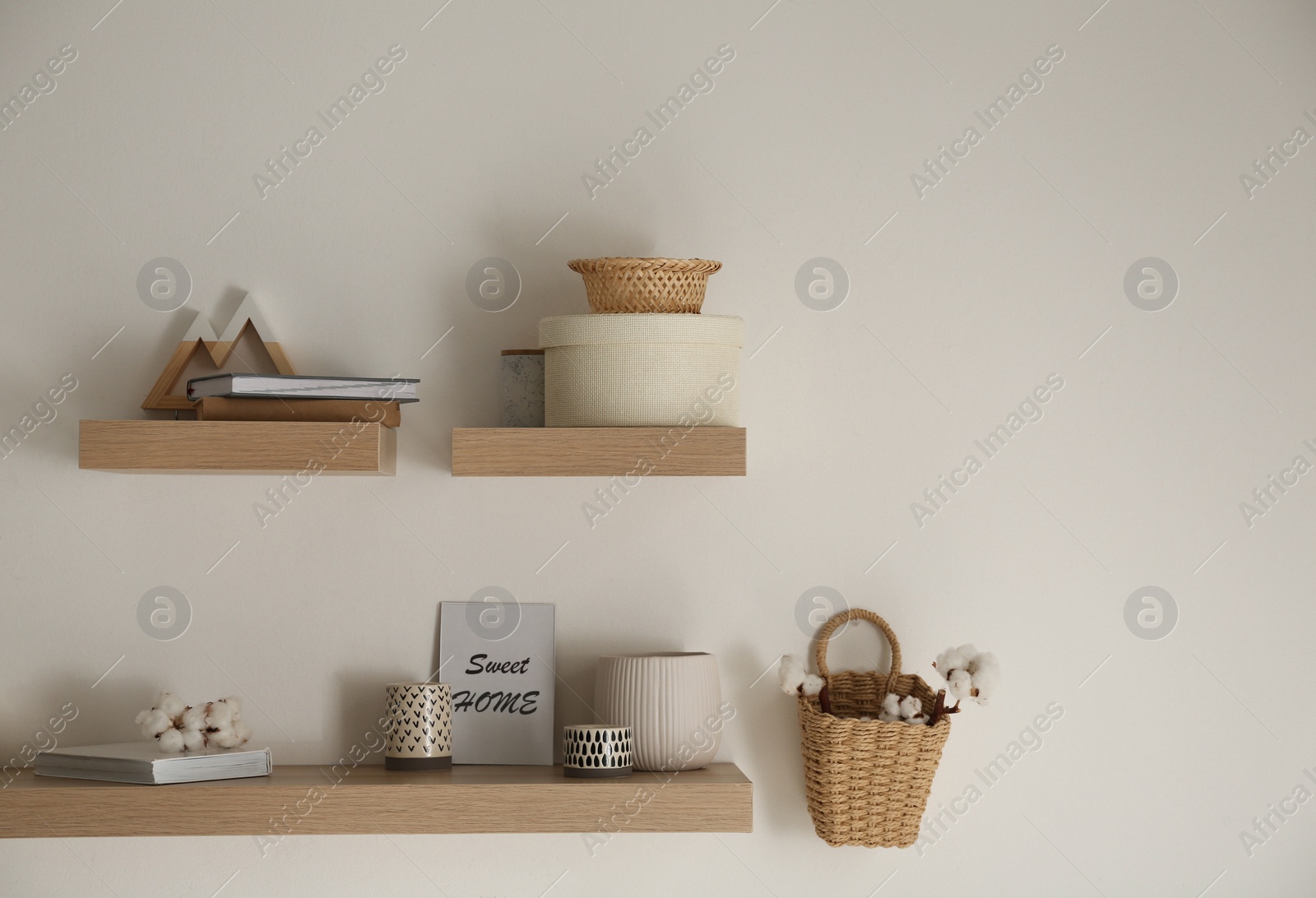 Photo of Wooden shelves with books and different decorative elements on light wall. Space for text