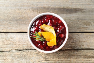 Photo of Fresh cranberry sauce in bowl, rosemary and orange peel on wooden table, top view