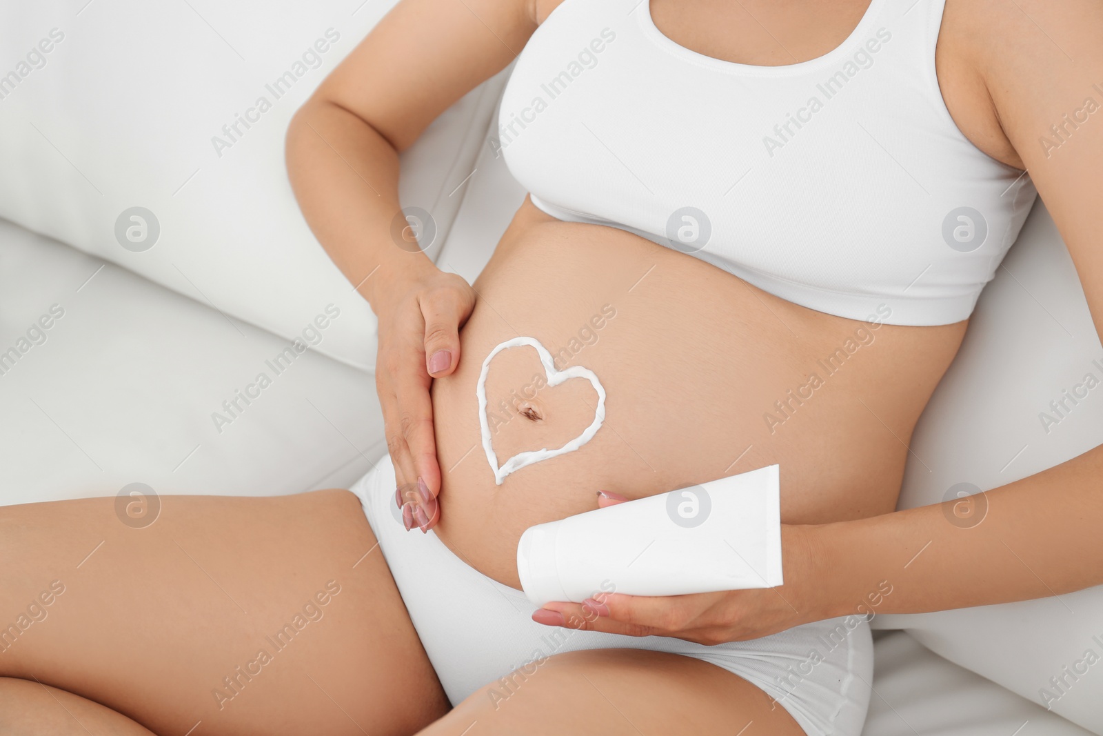 Photo of Heart painted with body cream on pregnant woman's belly at home, closeup