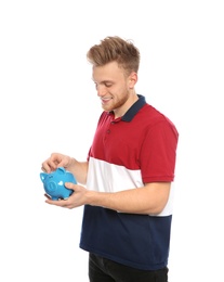 Young man putting coin into piggy bank on white background