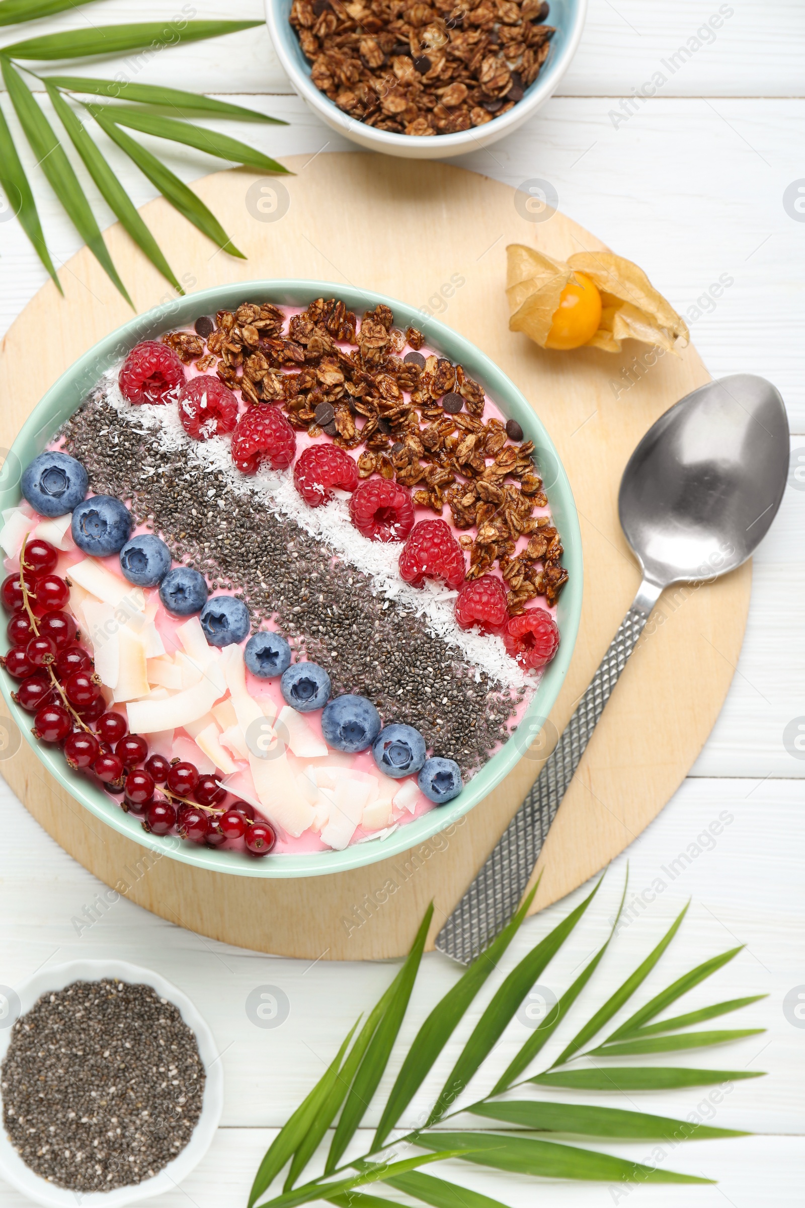 Photo of Tasty smoothie bowl with fresh berries and granola served on white wooden table, flat lay