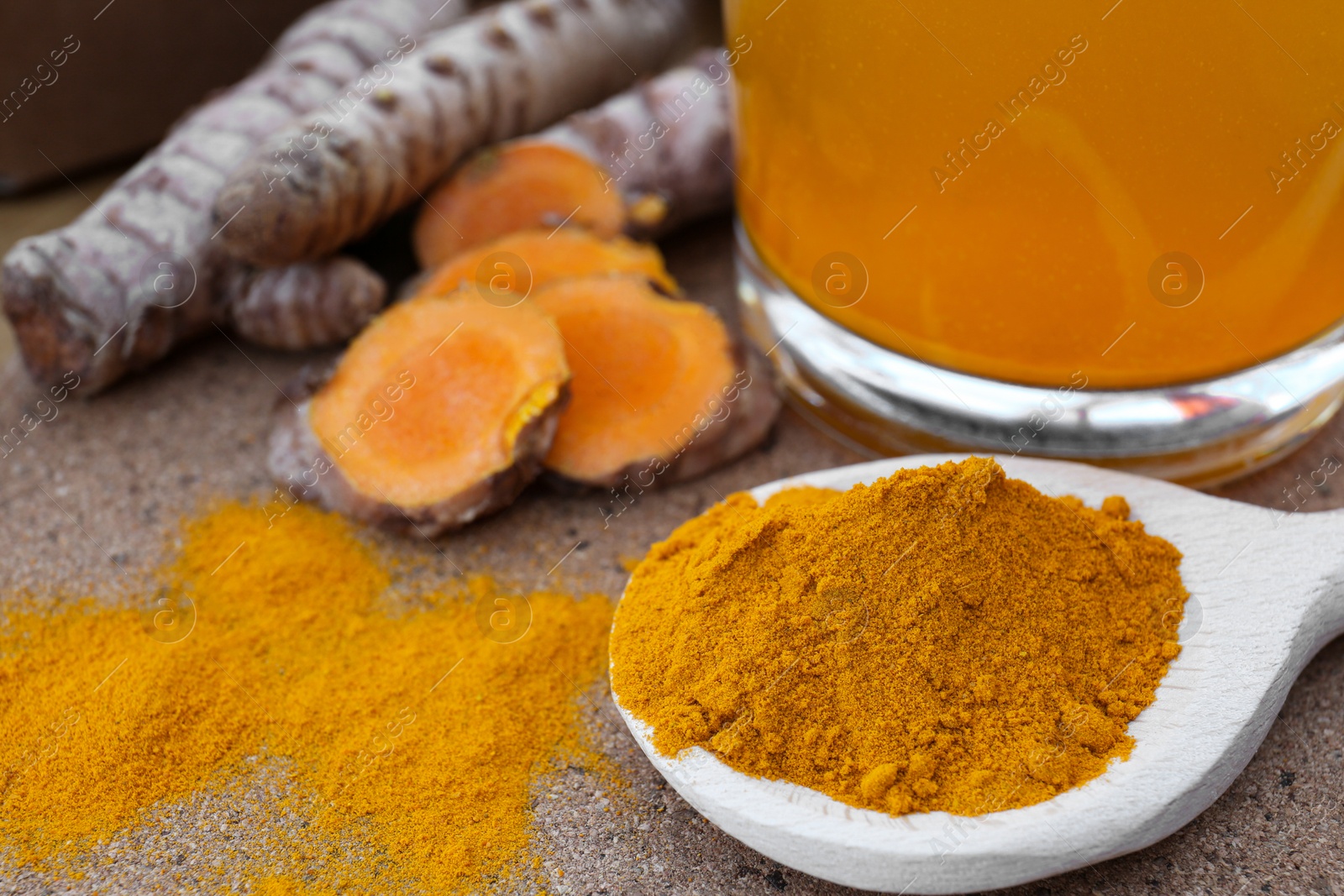 Photo of Glass cup of hot tea, turmeric powder and roots on wooden table, closeup