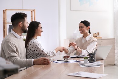 Real estate agent giving house key to young couple in office. Mortgage concept