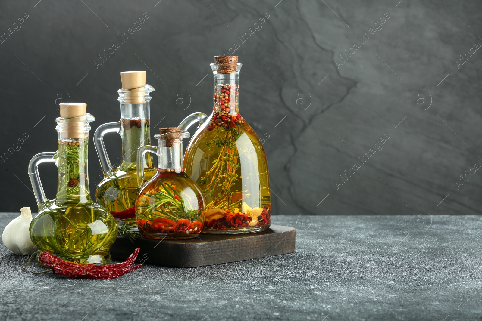 Photo of Cooking oil with different spices and herbs in jugs on light grey table. Space for text