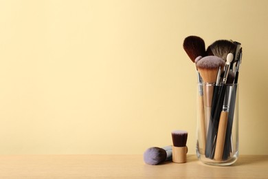 Photo of Set of professional makeup brushes on wooden table against beige background, space for text