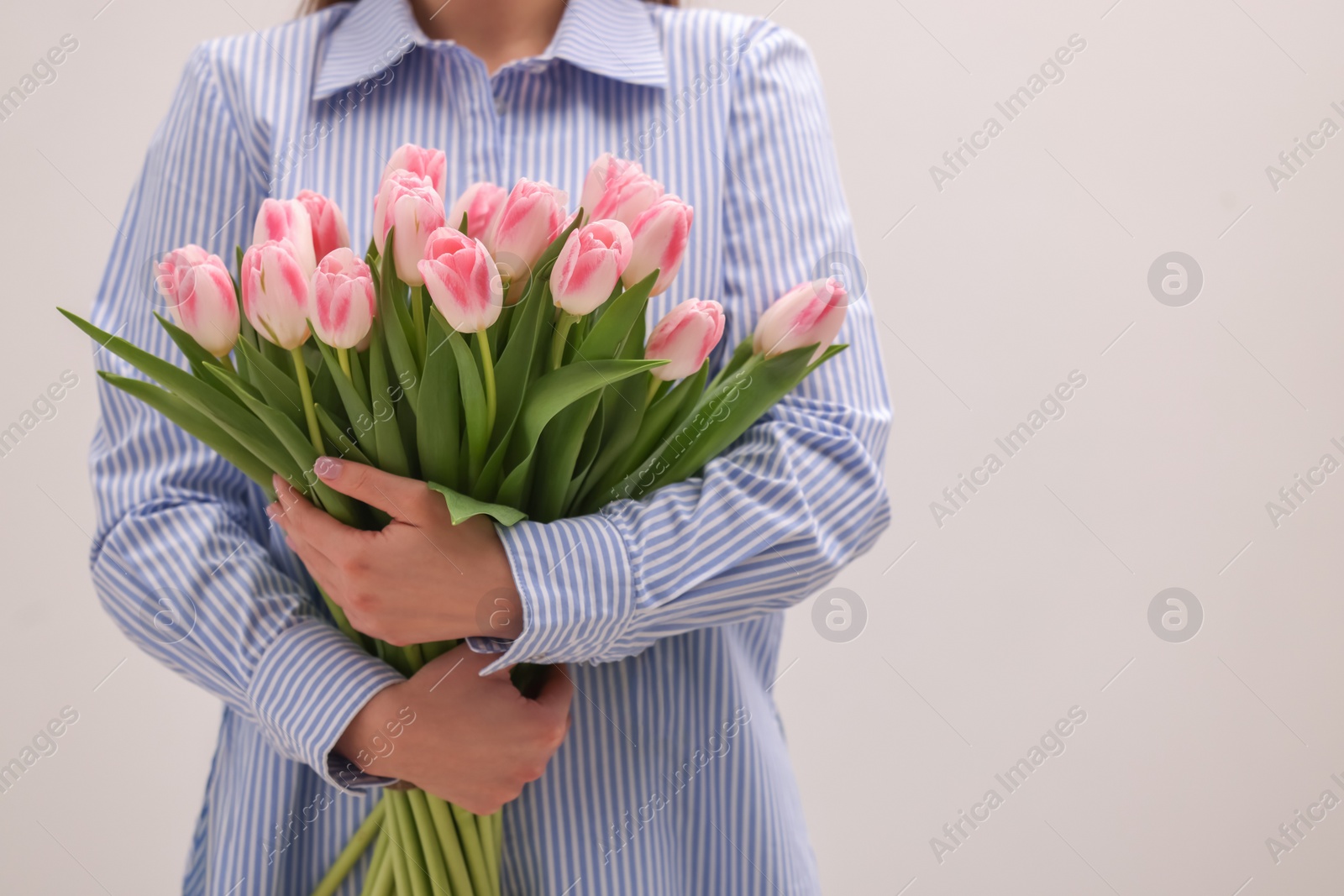 Photo of Woman with bouquet of beautiful fresh tulips on light grey background, closeup. Space for text