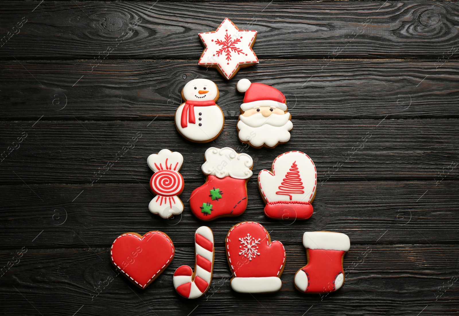 Photo of Christmas tree shape made of delicious decorated gingerbread cookies on black wooden table, flat lay
